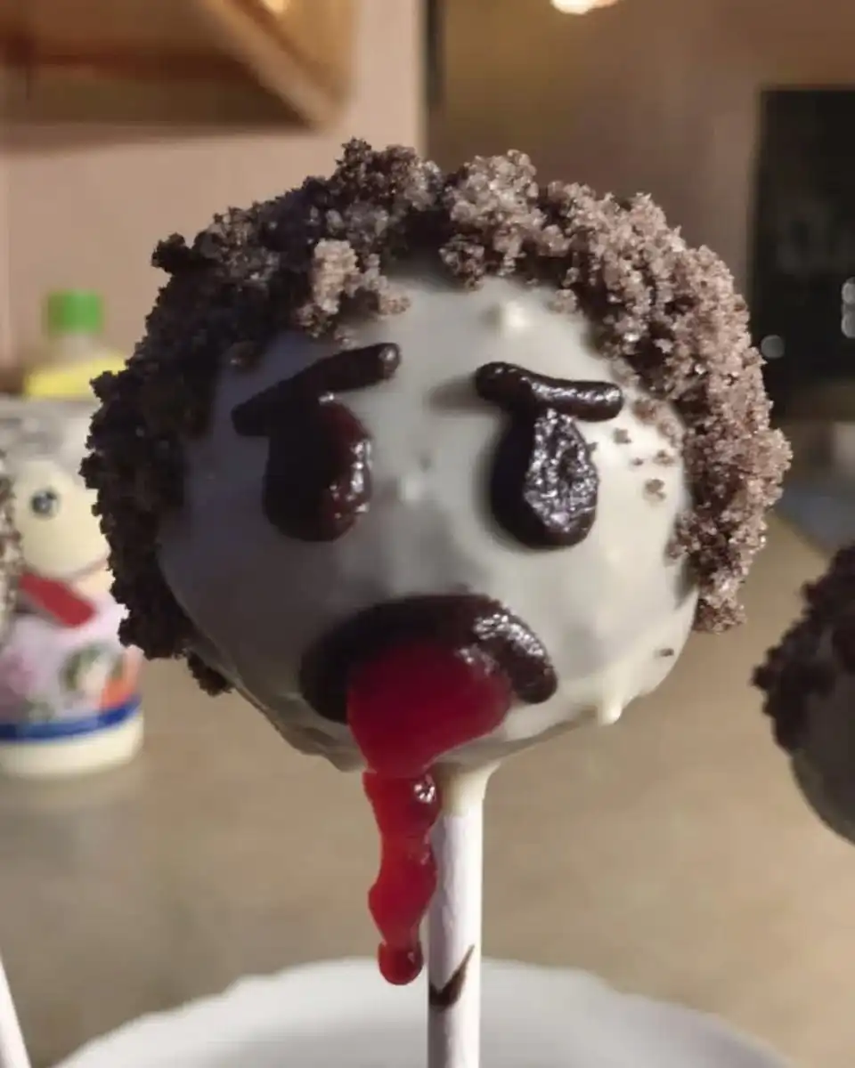 Hand dipping a cake pop into white melted chocolate