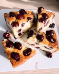 Whole fresh cherry cake on a rustic wooden table with scattered cherries