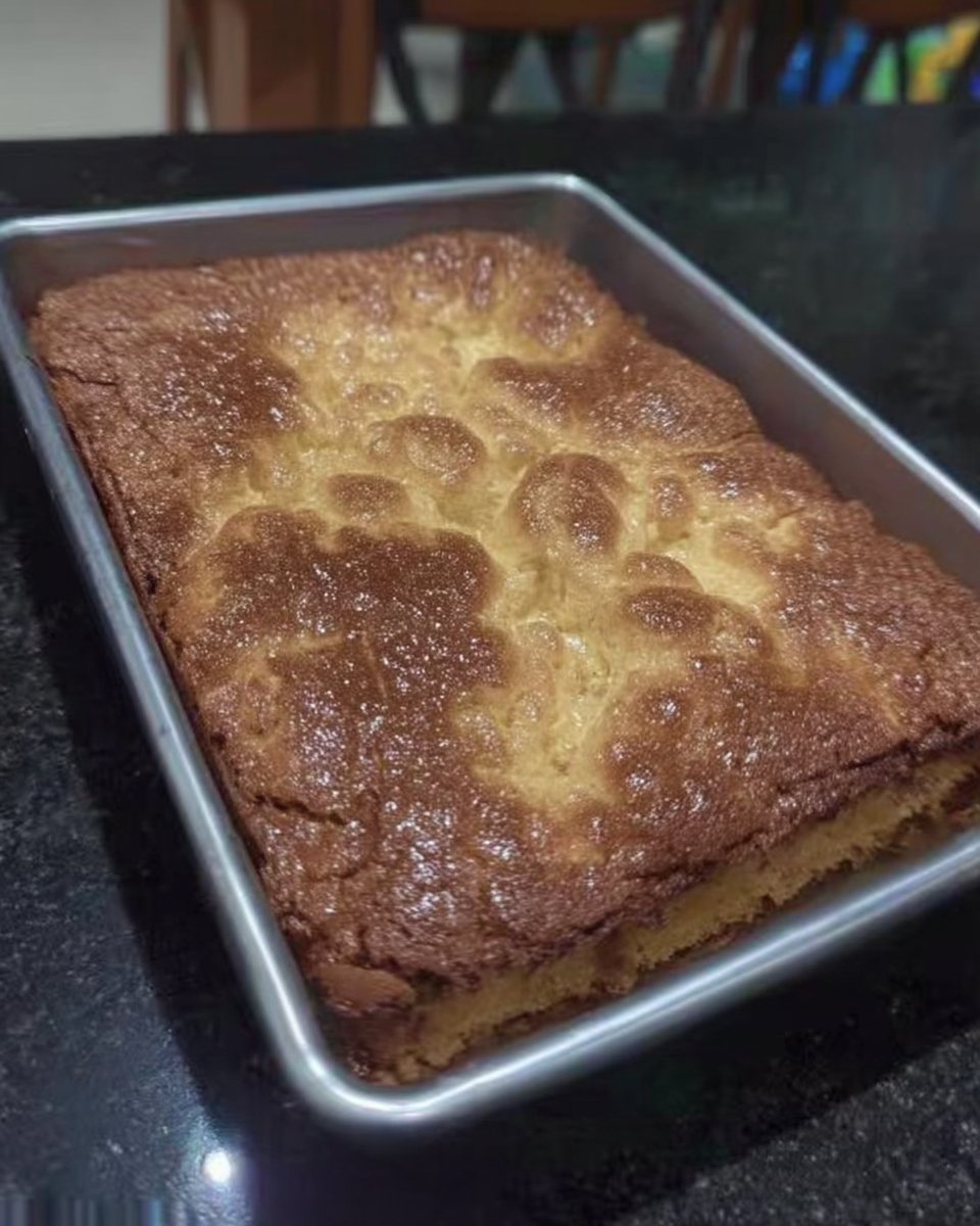 A golden brown ooey gooey butter cake in a glass baking dish showing the contrast between the crust and soft center.