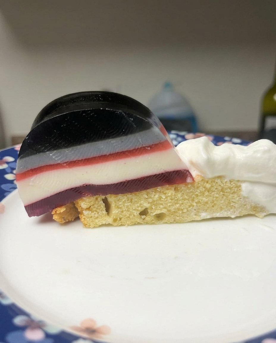 A close up of a slice of layered jello cake showing fruit and cream layers