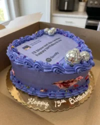 A four layer purple Olivia Rodrigo cake with a Spotify topper and ribbon bows