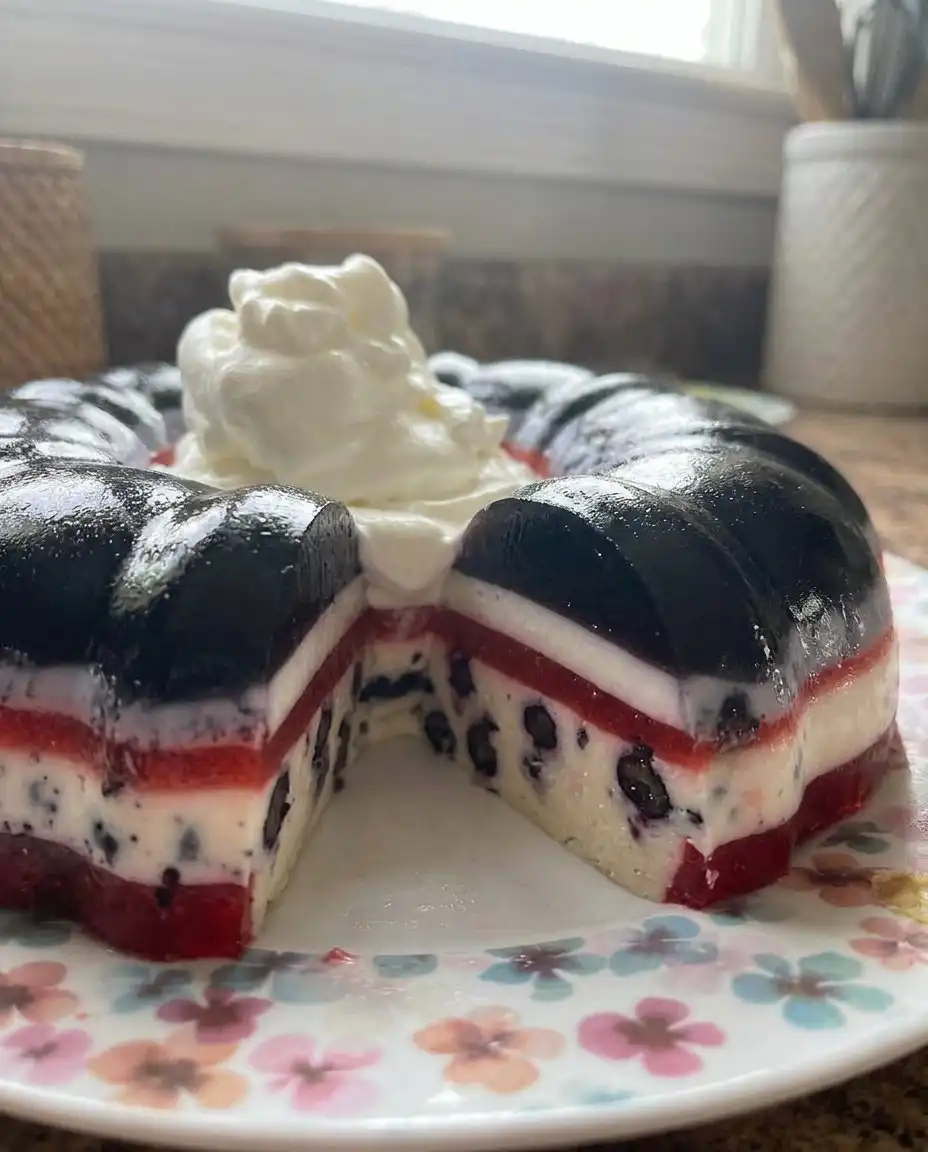 A slice of jello cake served on a white plate with mint and whipped cream