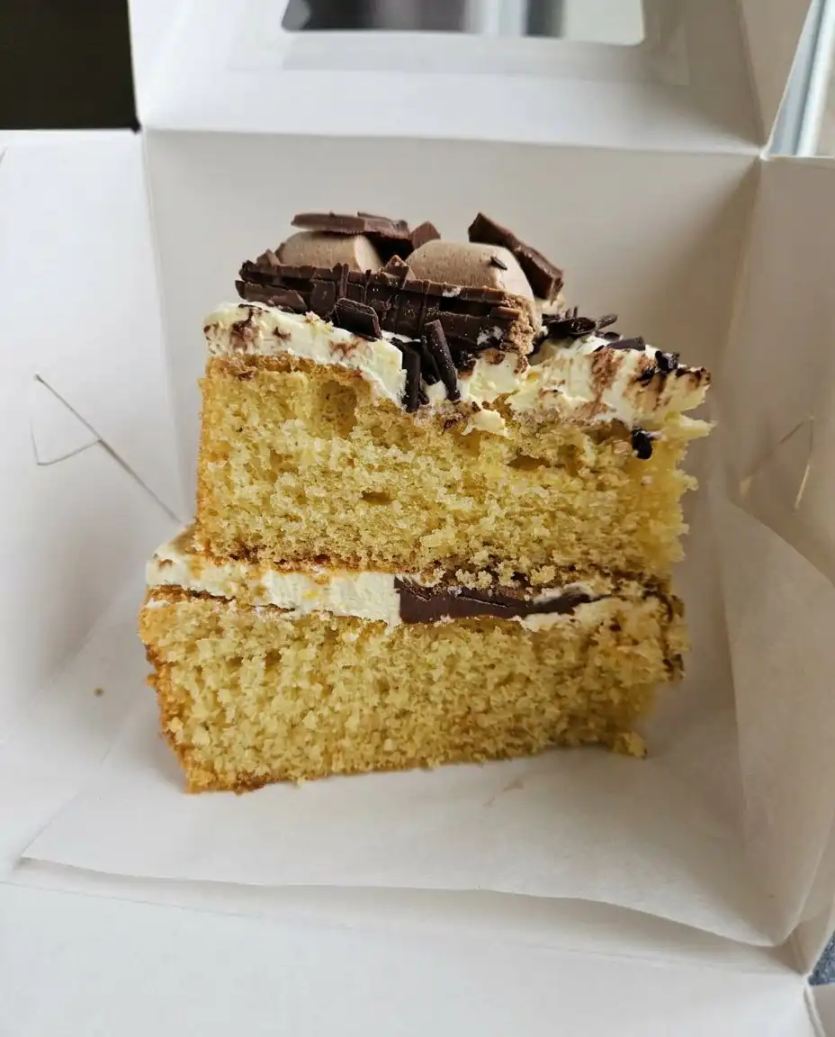 An offset spatula spreading thick white cream cheese frosting over a cooled carrot cake.