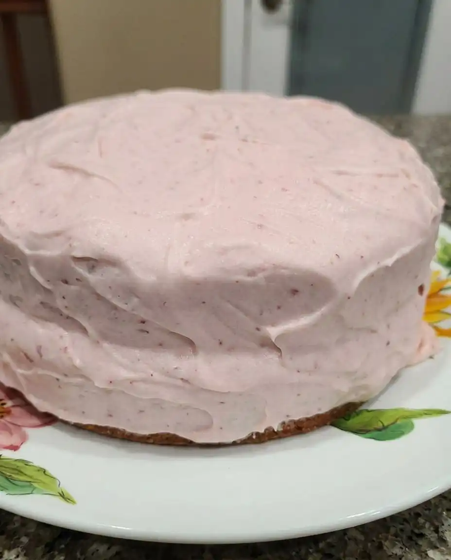 Fresh Strawberry Cake 10 A golden fresh strawberry cake topped with pink buttercream on a rustic wooden table.
