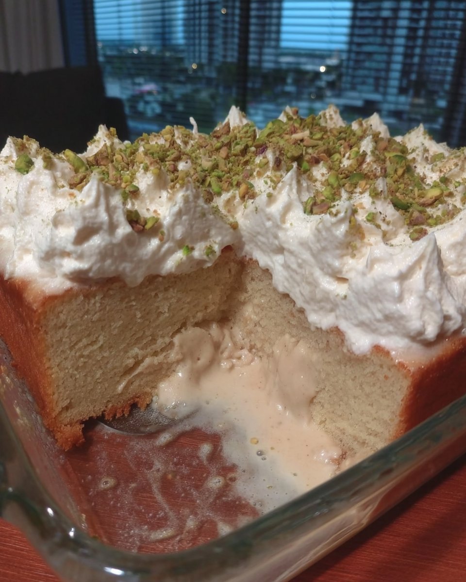 A slice of tres leches cake topped with whipped cream and a sprinkle of cinnamon on a white plate.