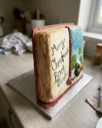 A rectangular book cake decorated with pink royal icing flowers on a rustic wooden table