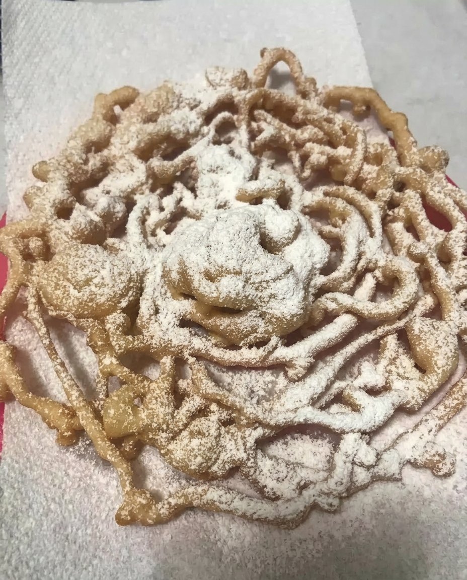 A golden brown funnel cake heavily dusted with powdered sugar on a plate