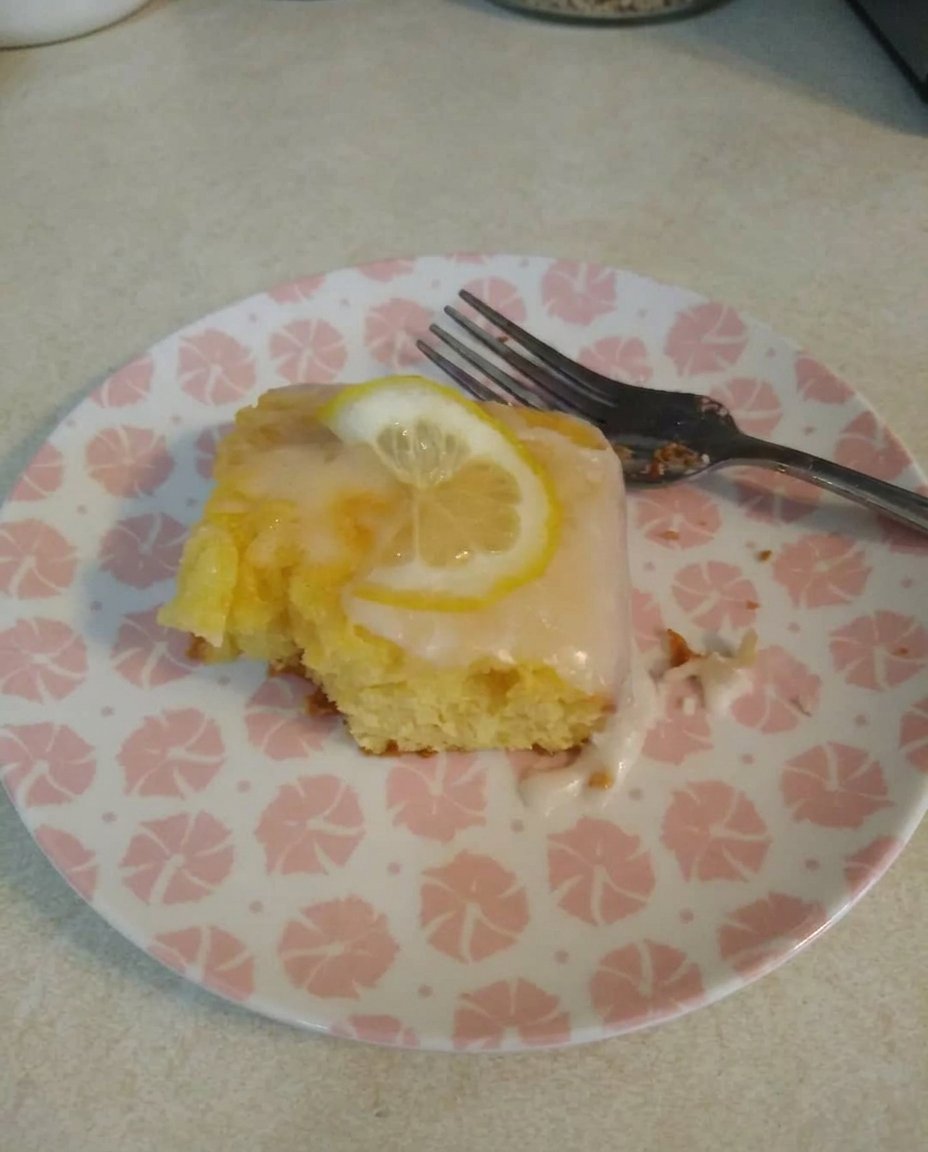 Close up of bright lemon glaze cascading into the holes of a warm baked sponge