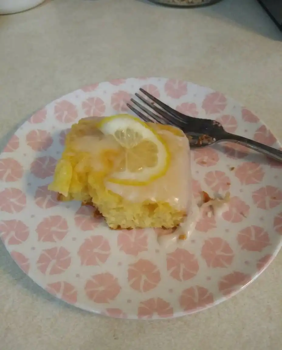 Close up of bright lemon glaze cascading into the holes of a warm baked sponge