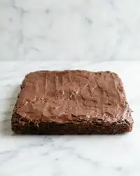 A close up shot of a moist chocolate zucchini cake with walnuts on a white plate.