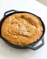 A warm Classic Peach Cobbler Dump Cake in a glass baking dish showing a golden crust and bubbling fruit.