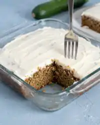 A moist slice of Classic Zucchini Cake with Cream Cheese Frosting sitting on a white plate.