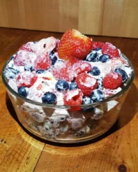 A large glass bowl filled with creamy red white and blue cheesecake salad topped with fresh berries