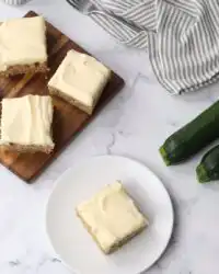 A close up view of several Zucchini Bars with thick cream cheese frosting on a plate.