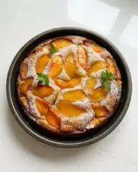 A golden brown fresh peach cake cooling on a wire rack with visible fruit layers.