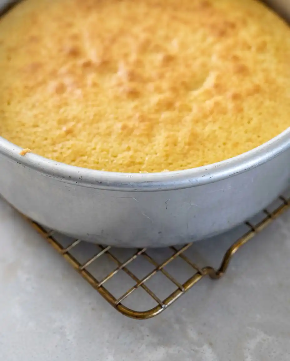 An offset spatula spreading chocolate frosting over a Classic Two-Layer Yellow Cake with Chocolate Frosting.
