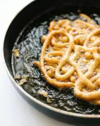 A golden brown Pumpkin Spice Funnel Cake dusted with powdered sugar on a white plate.