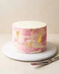 A beautiful Two-Layer Watercolor Buttercream Cake sitting on a white rotating cake stand.