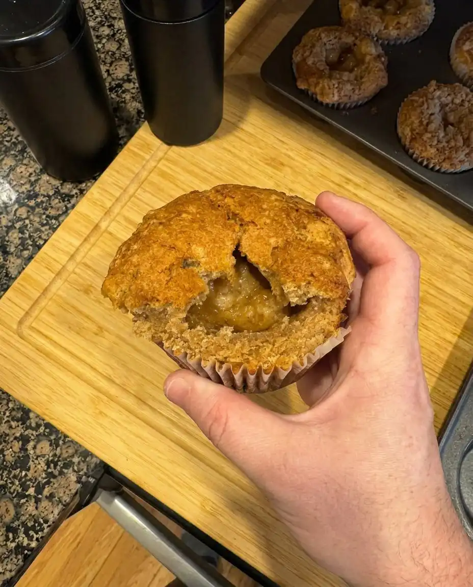 A peach cobbler muffin broken in half to show the moist crumb and juicy peach pieces