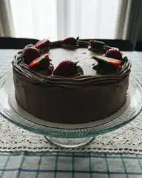 A four-layer strawberry chocolate cake with pink frosting and fresh berries