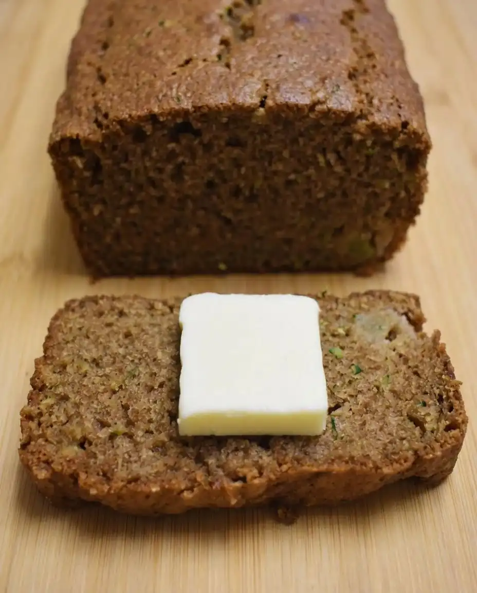 A slice of apple zucchini bread topped with a melting pat of yellow butter.