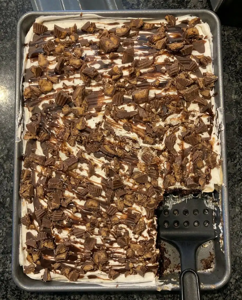 A slice of Reese’s Peanut Butter Cup Poke Cake on a plate with fluffy whipped topping and candy pieces