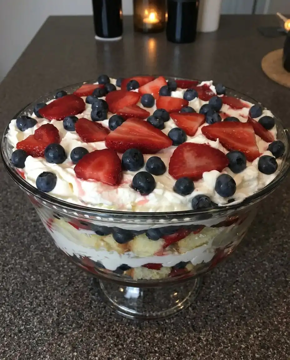 A pastry chef spreading stabilized whipped topping over a layer of fresh berries in a trifle bowl.