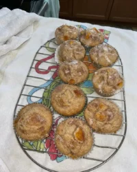 A tray of freshly baked Homemade Peach Cobbler Muffins 2 with golden streusel tops