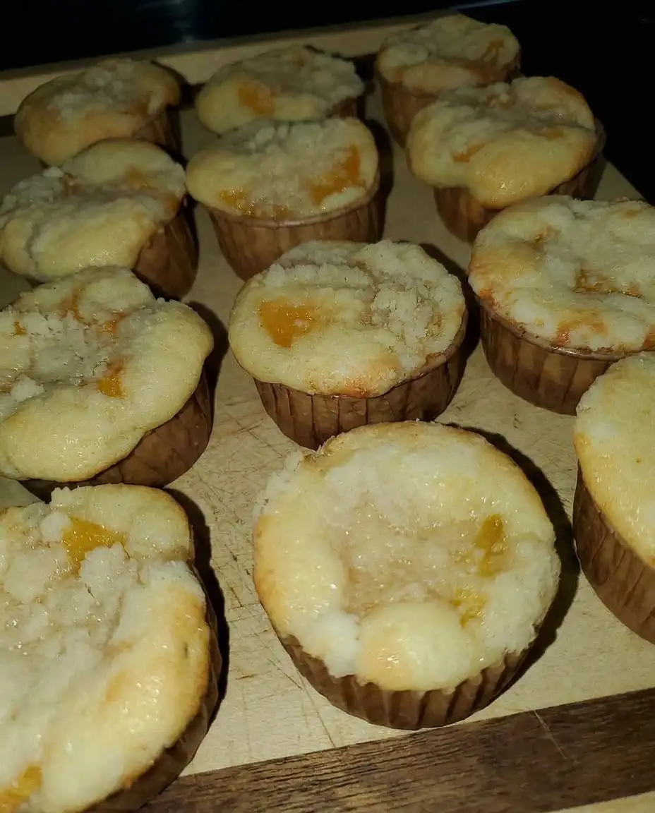 Two warm peach muffins on a plate with a small pat of melting butter