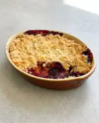A golden brown Blackberry Apple Dump Cake bubbling in a white ceramic dish