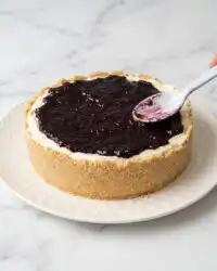 A beautiful close-up of a Blackberry Cream Cheese Cake with a thick graham cracker crust and purple topping.