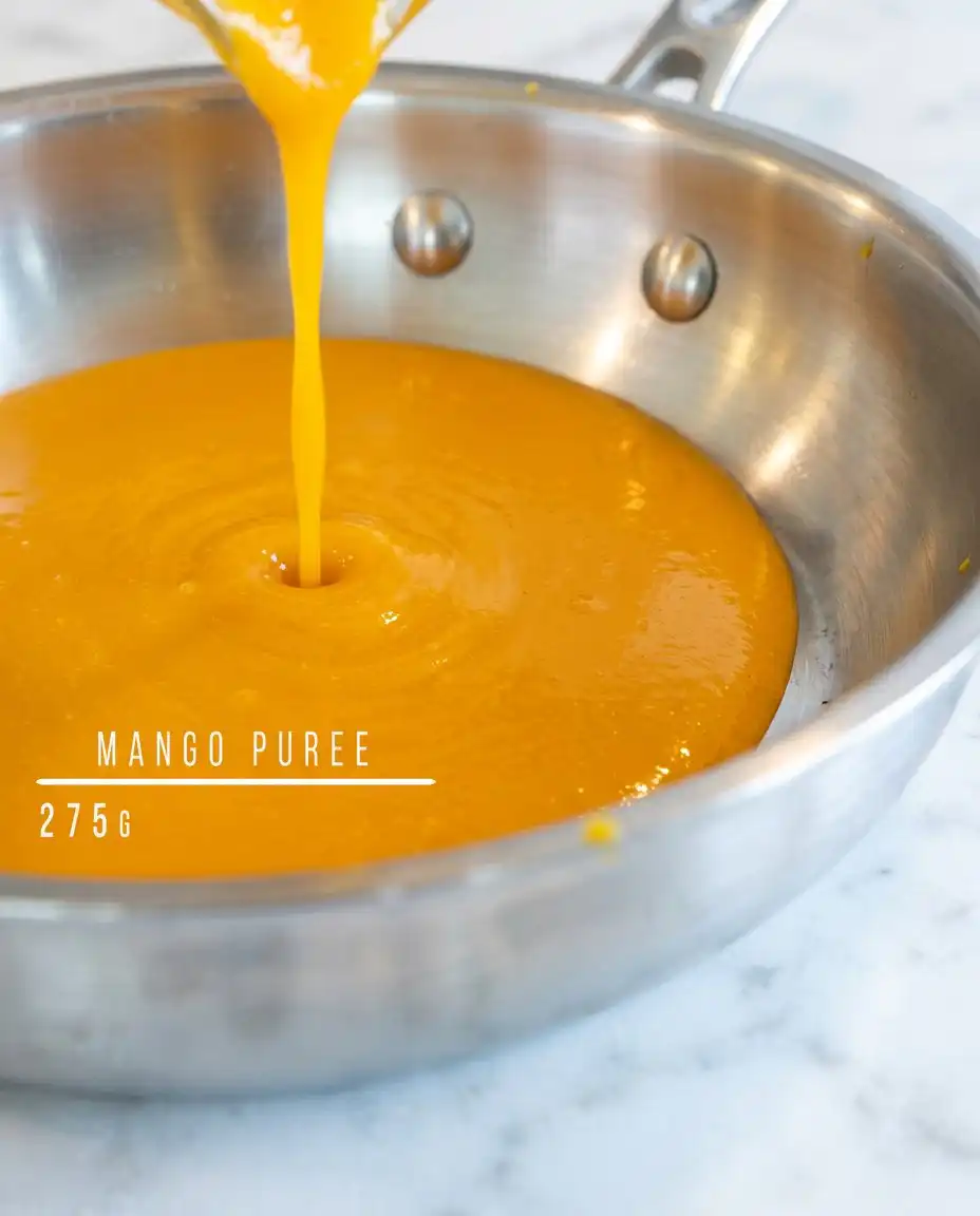 A hand gently folding whipped cream and mango puree for Classic Mango Mousse Cake.