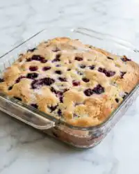 A golden brown Blueberry Buttermilk Breakfast Cake resting in its baking pan on a rustic wooden table.