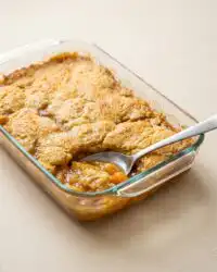A golden brown Cinnamon Canned Peach Dump Cake bubbling in a ceramic baking dish.