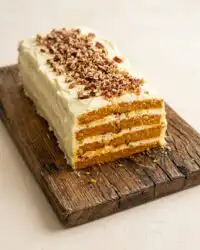 An elegant Classic Pumpkin Layer Cake resting on a wire cooling rack on a wooden bench.