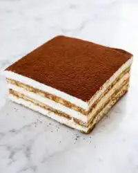 A perfectly sliced piece of Classic Tiramisu Layer Cake showing distinct sponge and mascarpone cream layers.