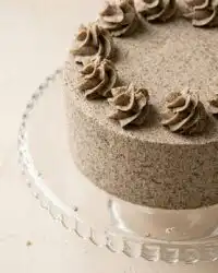 An elegant cookies and cream birthday cake topped with swirls and whole cookies on a glass stand