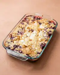 A warm slice of blackberry dump cake with butter pecan cake mix served in a shallow white ceramic bowl.