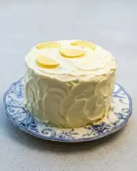 A tall three layer Lemon Blueberry Layer Cake with Cream Cheese Frosting decorated with fresh blueberries.