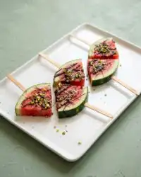Frozen Watermelon Teething Pops lined up on a parchment paper lined baking sheet.