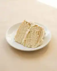 A gorgeous Two-Layer Buttermilk Cake covered in creamy white frosting on a cake stand.