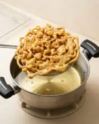 Pouring batter through a funnel to make a golden brown 3-Ingredient Funnel Cake in hot frying oil.