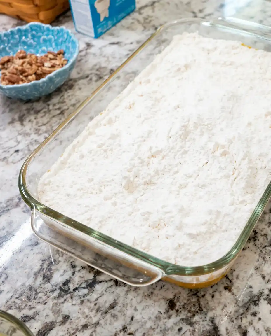 Classic Pumpkin Crunch Cake 15 Pouring melted butter over dry cake mix and pecans for Classic Pumpkin Crunch Cake.