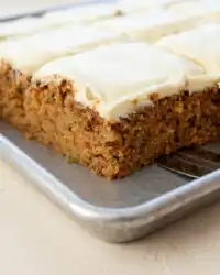 A tender slice of homemade Zucchini Spice Cake topped with thick cream cheese frosting on a rustic plate.