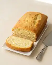 A golden brown cream cheese pound cake dusted with powdered sugar on a white cake stand.
