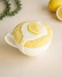 A warm lemon mug cake dusted with lemon zest and sweet glaze in a rustic mug