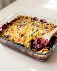 A warm spoonful of 3-Ingredient Blueberry Dump Cake served with melting vanilla ice cream on a white plate