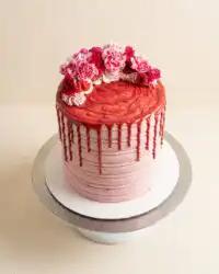 A beautiful White Chocolate Raspberry Anniversary Cake decorated with fresh raspberries on a white stand.
