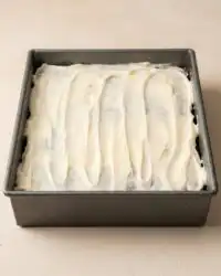 A sliced zucchini cake with applesauce topped with smooth cream cheese frosting on a wire rack.