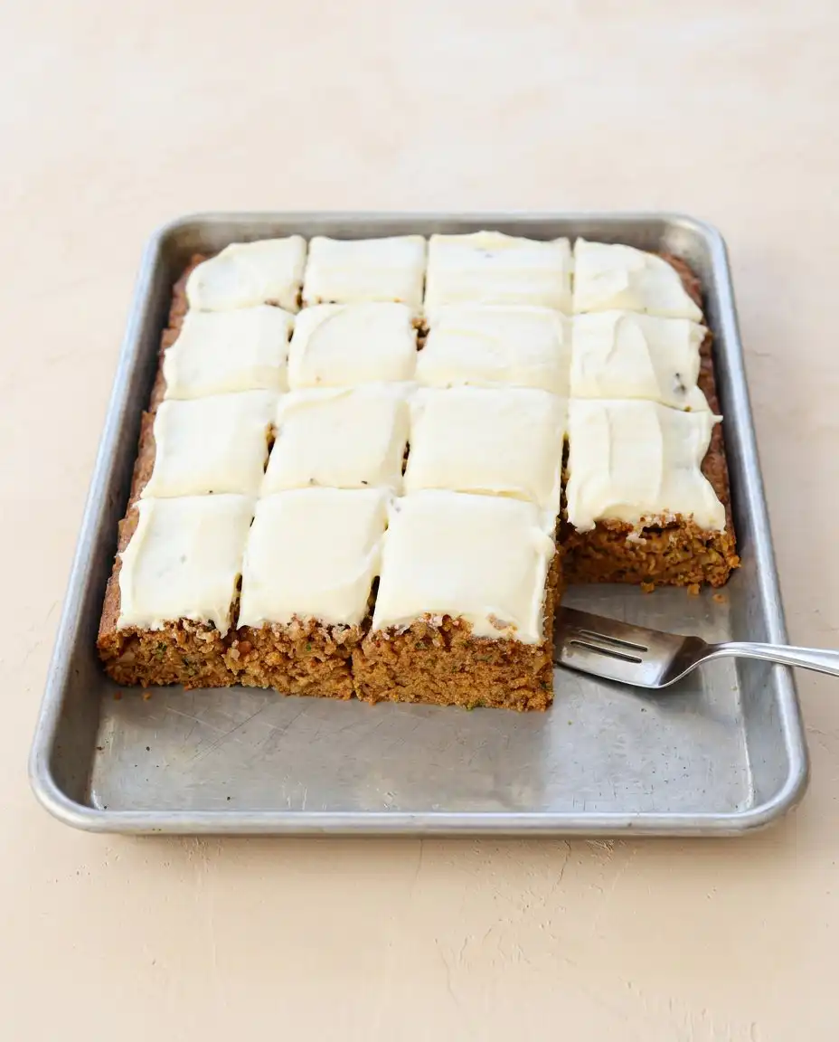 A whole frosted Zucchini Spice Cake served on a wooden board next to a cup of dark coffee.